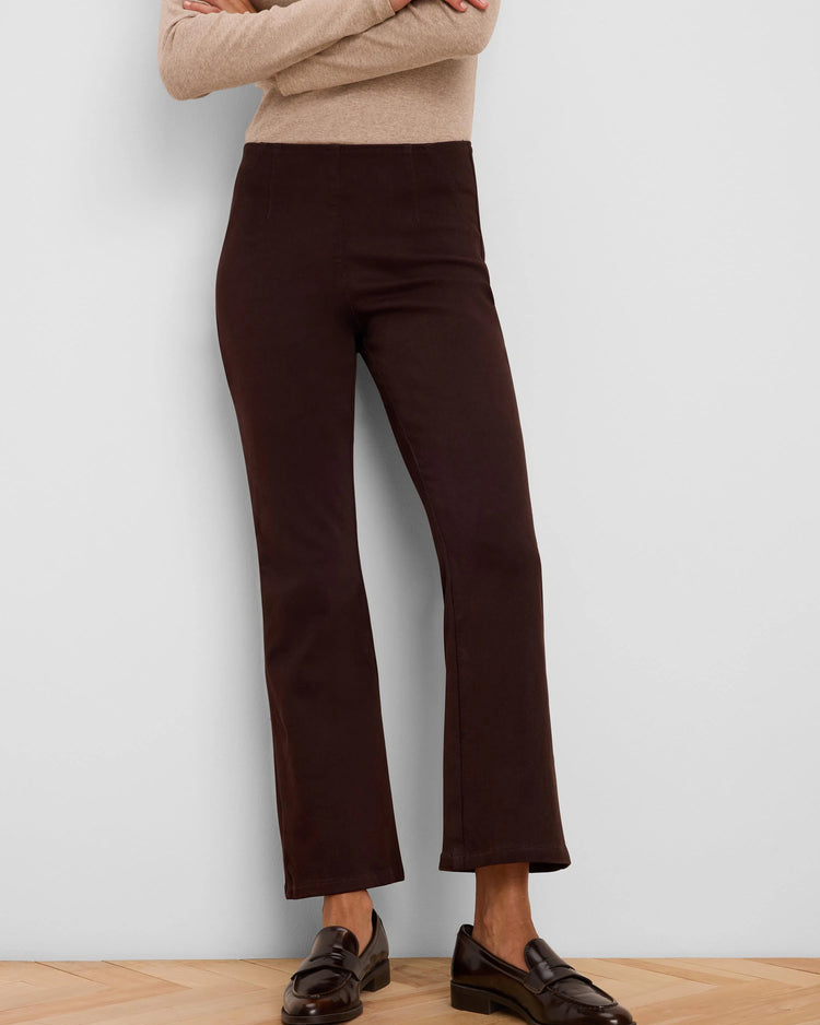 A model wearing dark brown cropped flare pants, a beige long-sleeve knit top, and dark brown leather loafers, standing against a light gray wall on a light wood parquet floor.