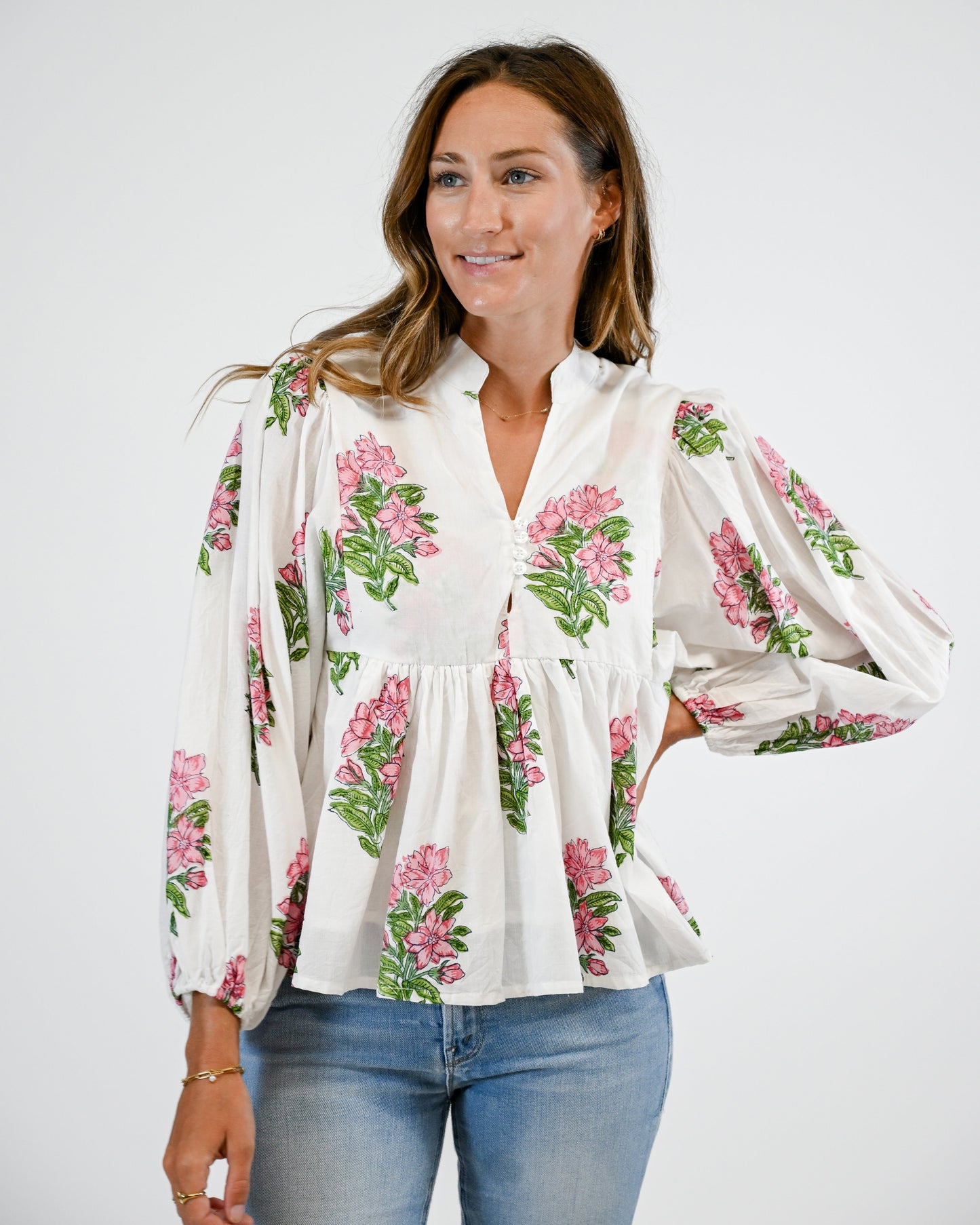 Woman wearing a white blouse with floral patterns and blue jeans on a white background