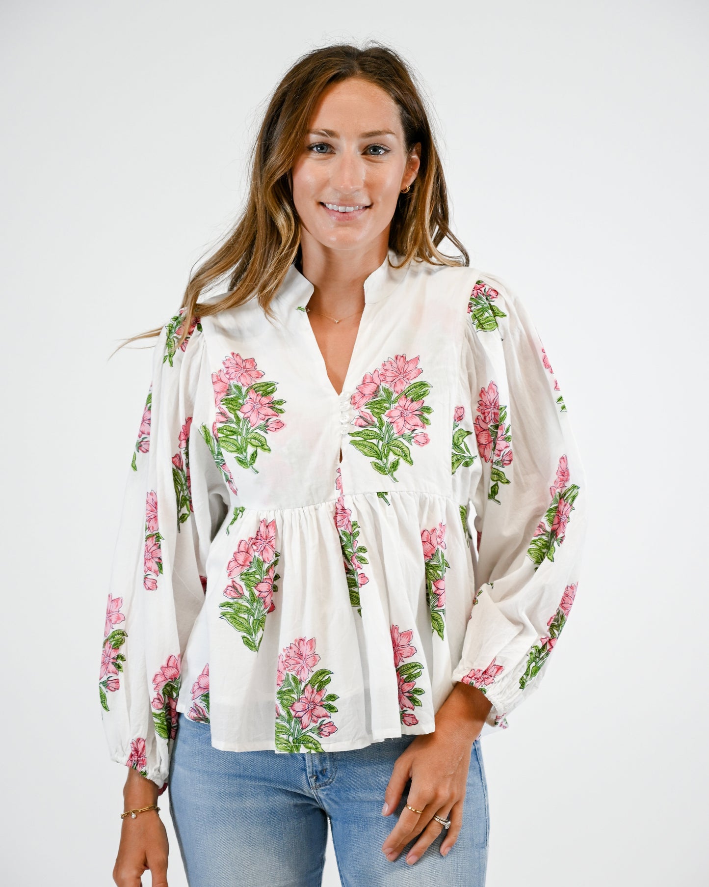 Woman wearing a white floral blouse with pink and green flowers on a plain background