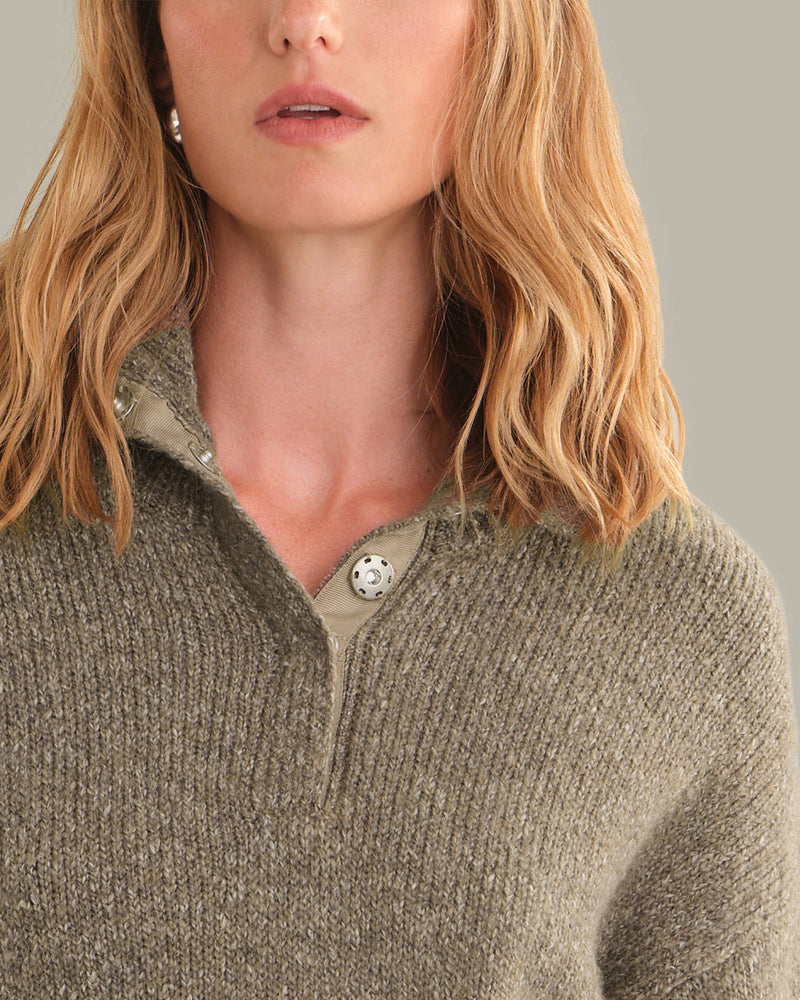 Close-up of a woman wearing a ribbed knit polo sweater in a heathered taupe-brown color, featuring a buttoned collar and a small silver earring.