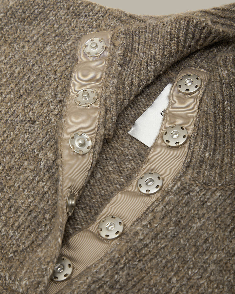 Close-up of a brown textured knit sweater featuring a beige ribbed trim with decorative silver-tone metal buttons.