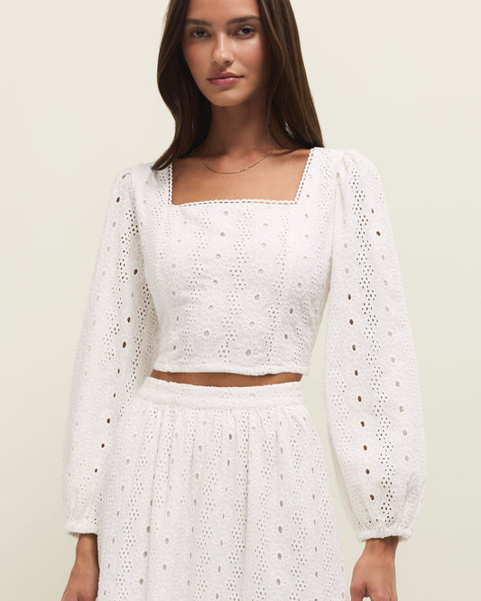 Woman wearing a white crochet outfit against a plain background