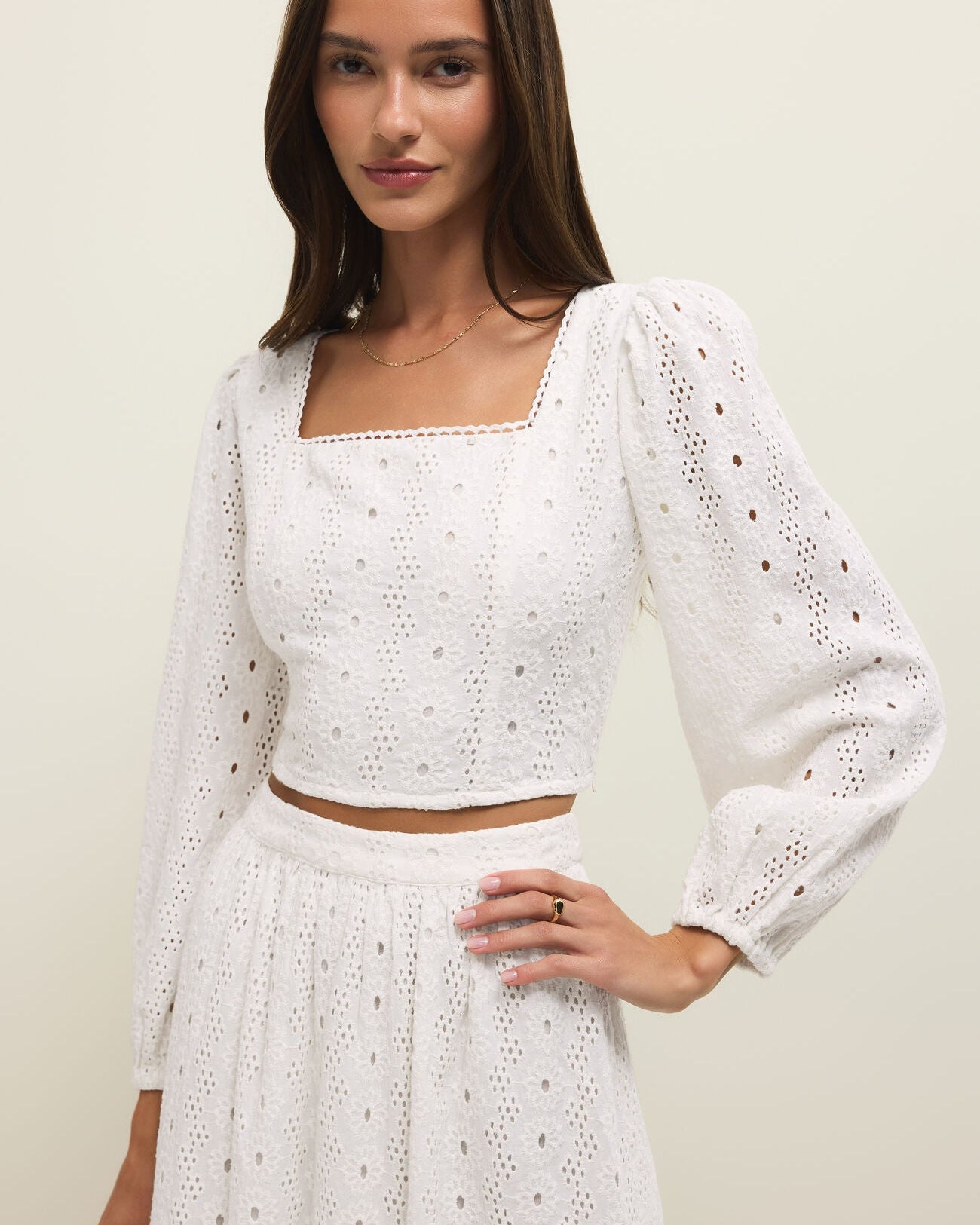 Woman wearing a white crochet outfit on a plain background