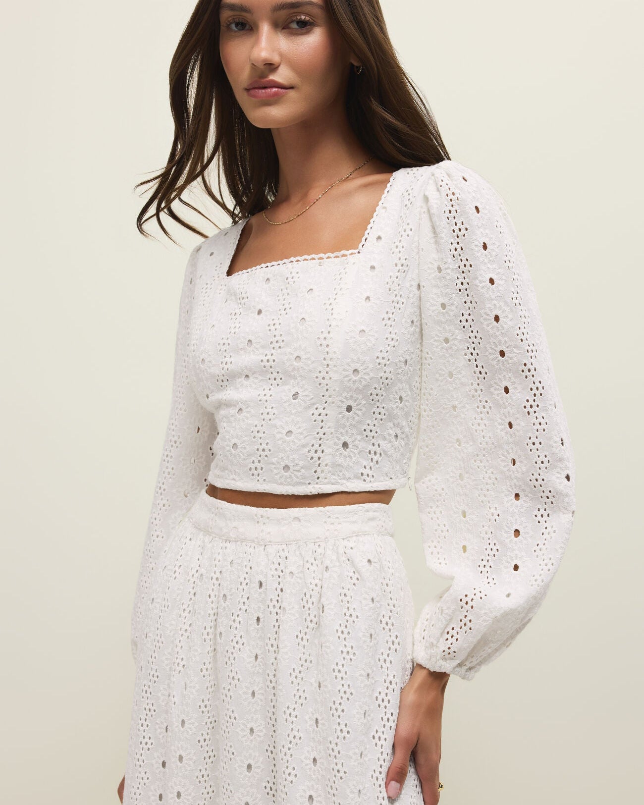 Woman wearing a white embroidered outfit against a plain background