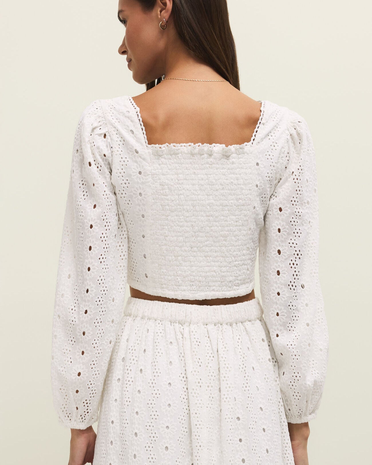 Woman wearing a white lace dress with long sleeves on a plain background