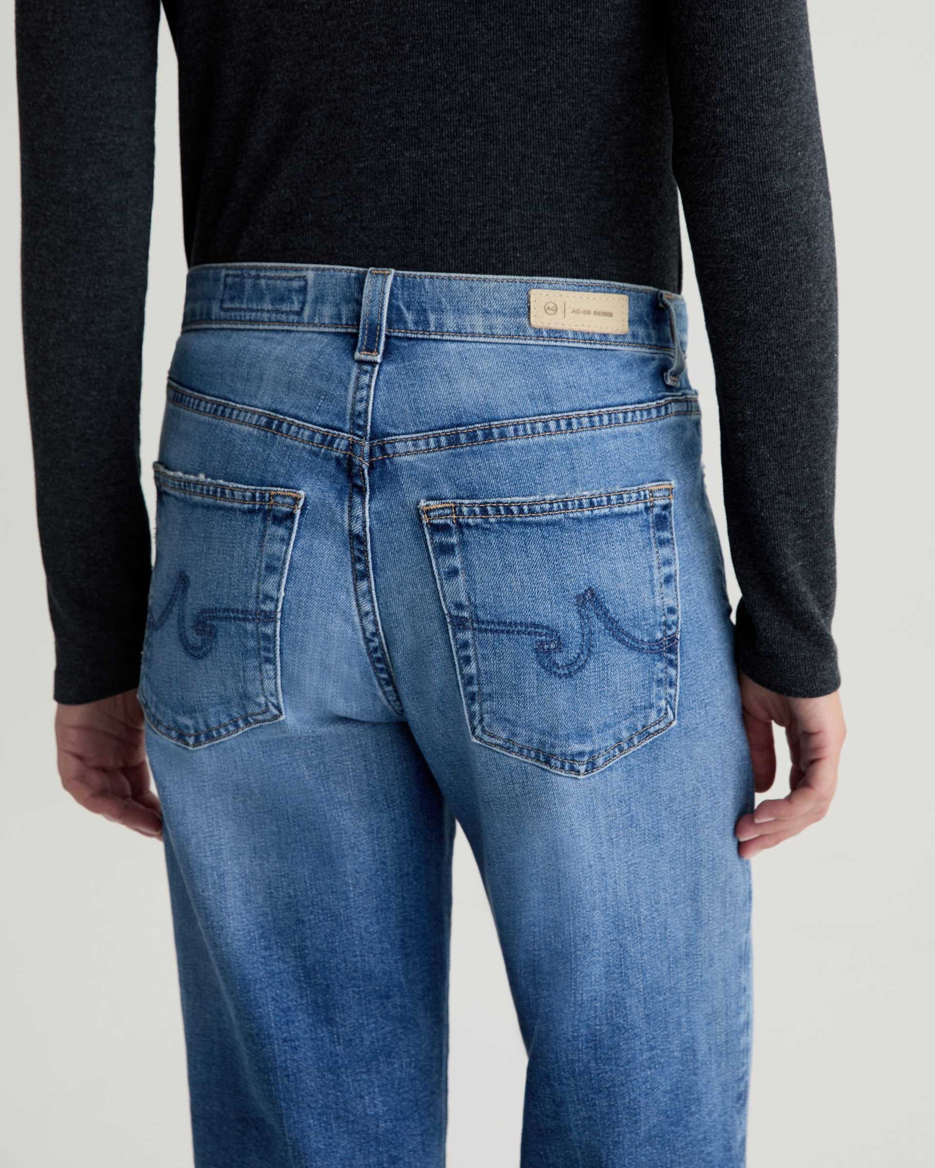 Person wearing blue jeans with a visible brand label on a plain background