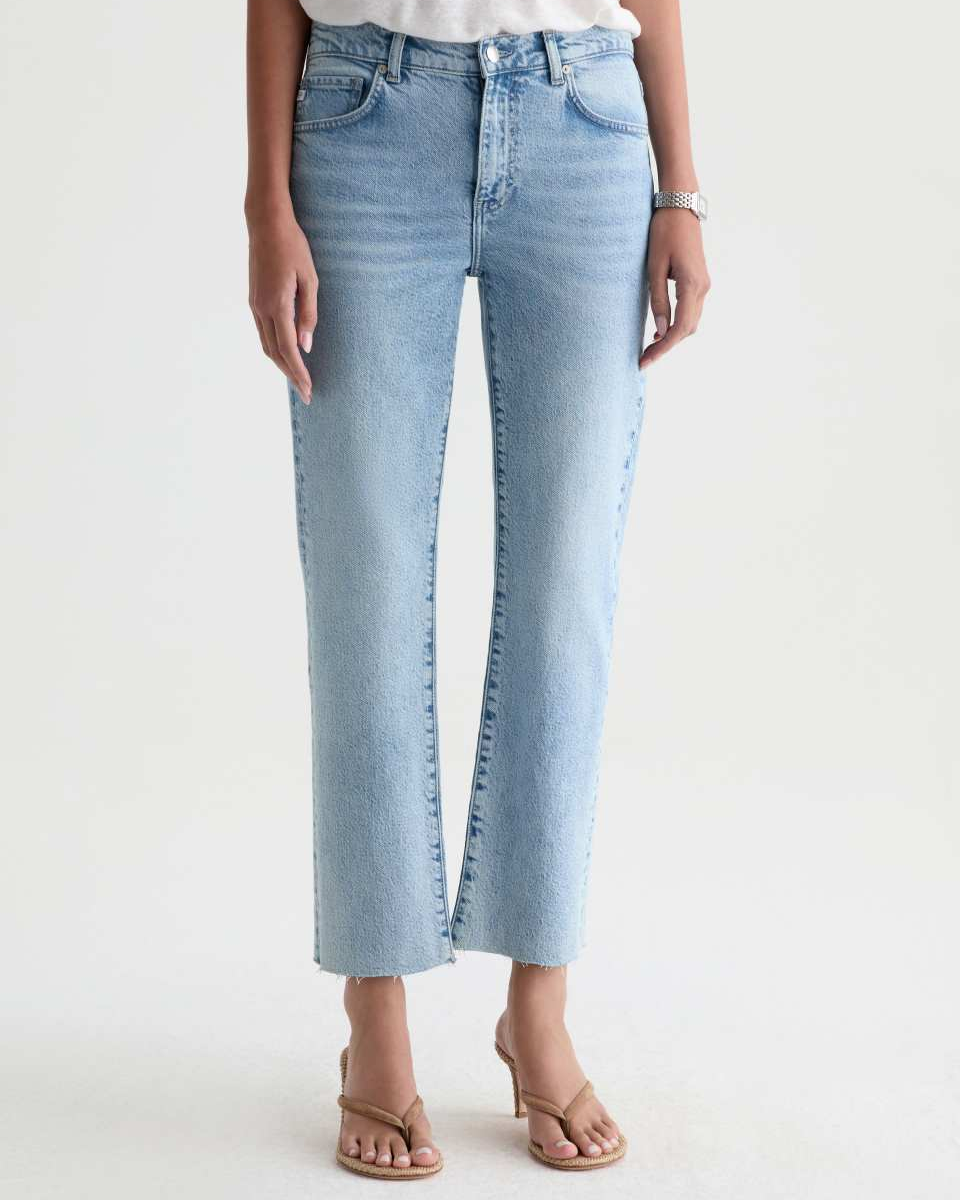 A model wearing light-wash blue cropped jeans with a straight-to-slightly-flared leg, paired with a white top and tan heeled sandals against a plain white studio background.