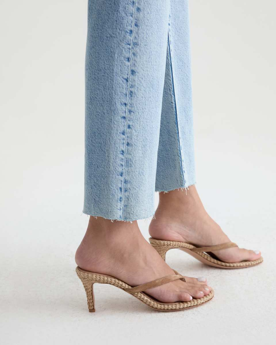 A person wearing light blue cropped jeans and tan woven-look heeled thong sandals with low block heels, shown from the calves down on a clean light gray studio background.