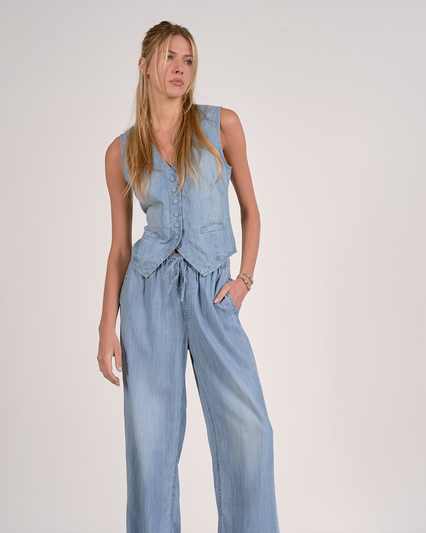 Woman wearing a light blue denim jumpsuit against a plain background