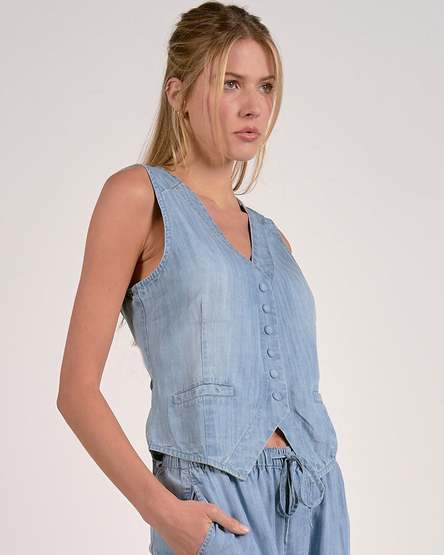 Woman wearing a light blue denim sleeveless top and pants on a plain background