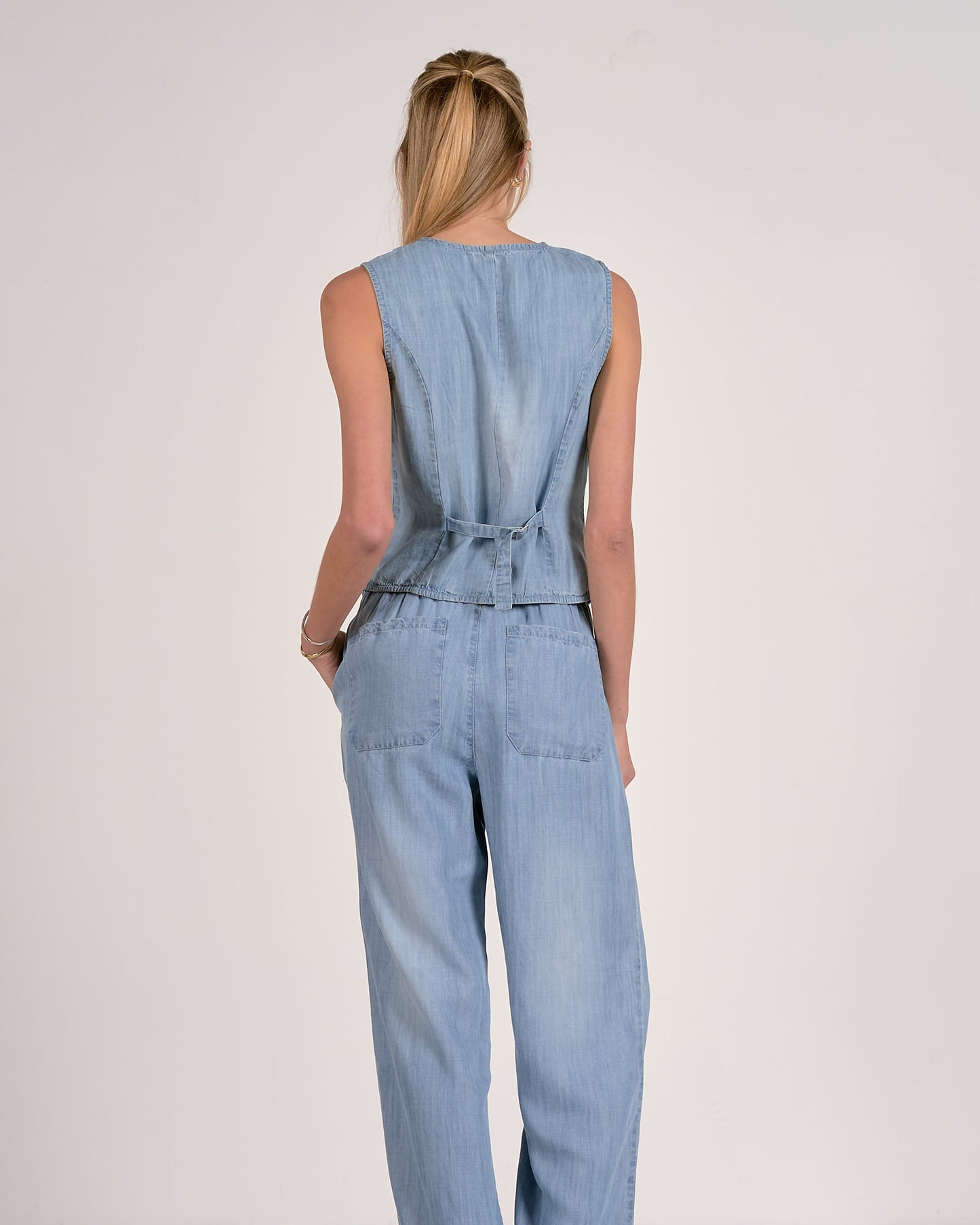 Woman wearing a light blue denim jumpsuit on a plain background