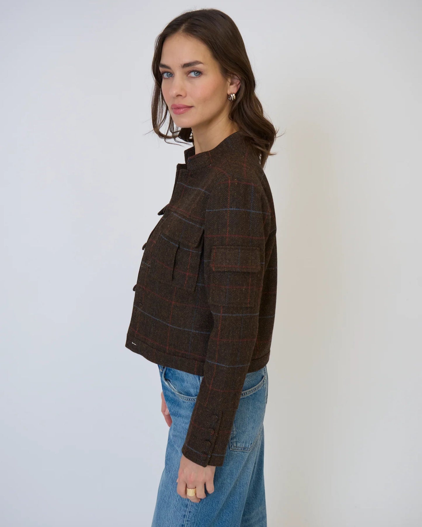 Woman wearing Central Park West Eden plaid military jacket in brown standing in front of a white background