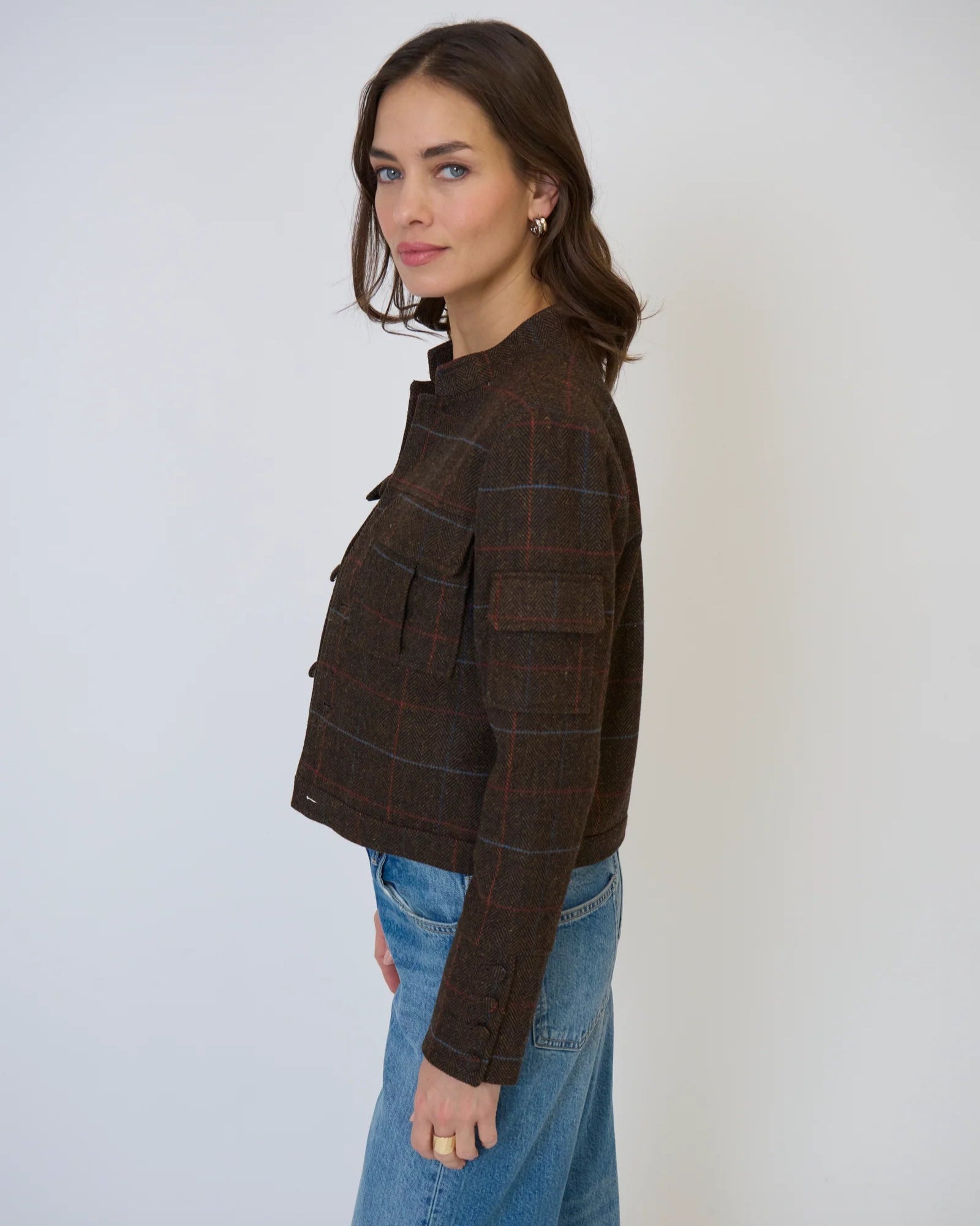 Woman wearing Central Park West Eden plaid military jacket in brown standing in front of a white background