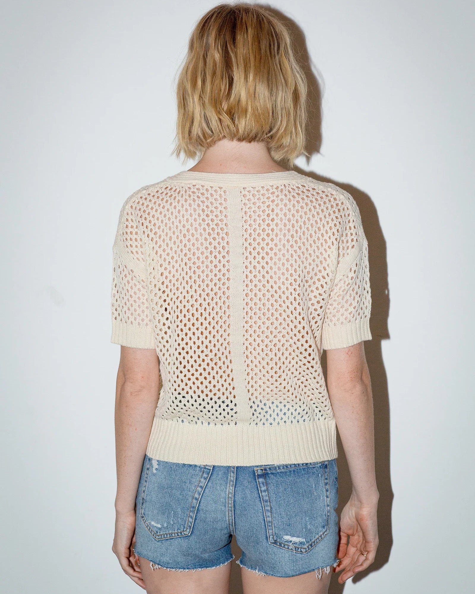 Person wearing a beige mesh top and denim shorts against a white background