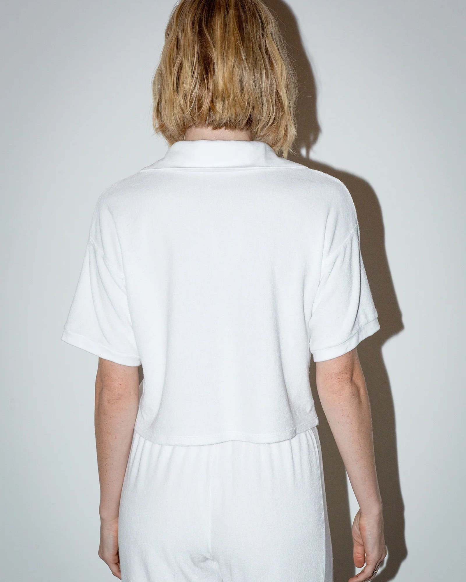 Person wearing a white shirt and pants against a plain background