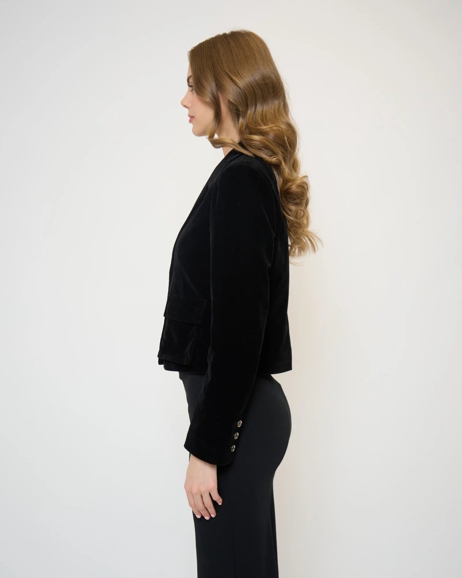 Side view of a model wearing a velvet jacket and black pants in front of a white background