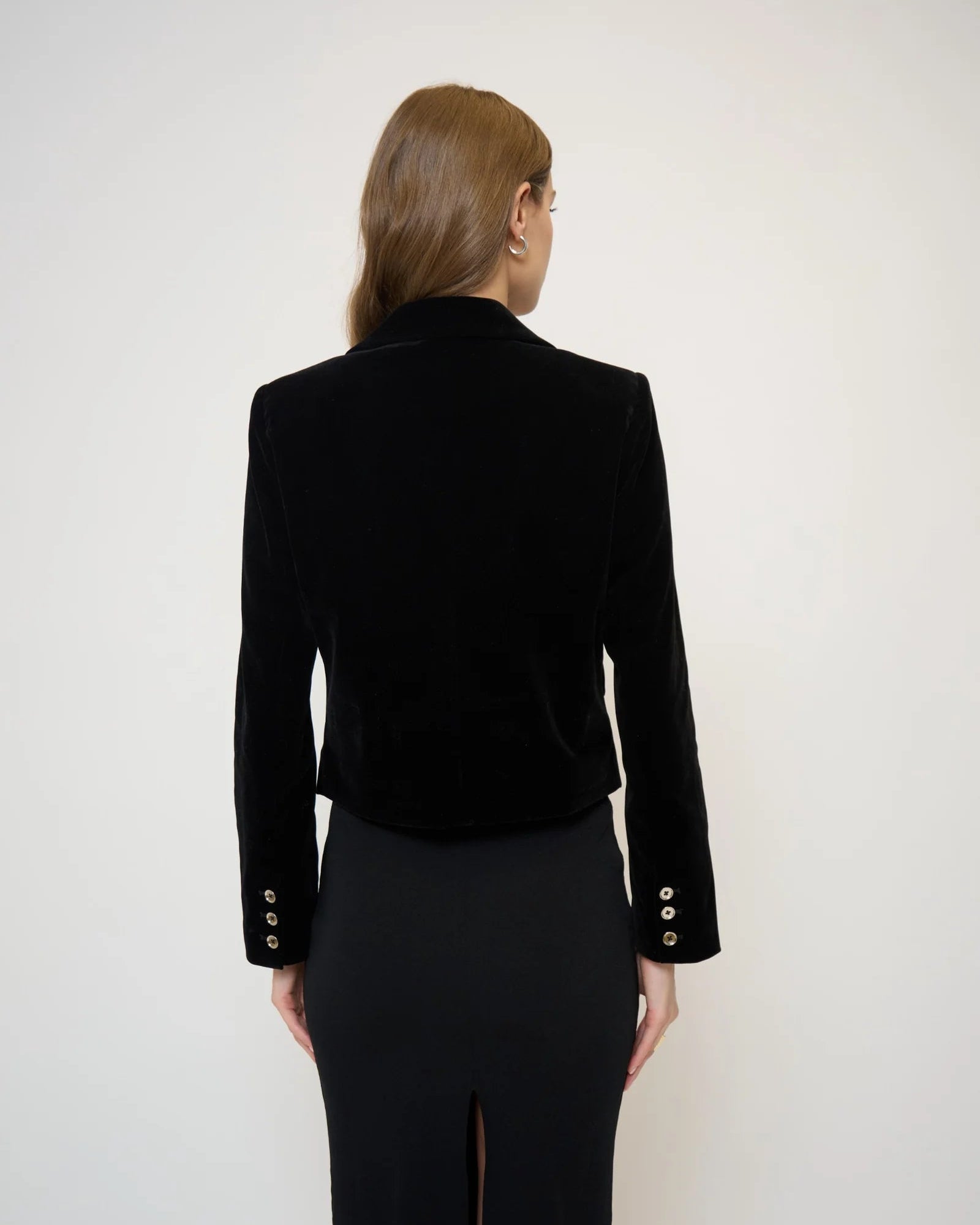 Back view of a model wearing a velvet jacket and black skirt in front of a white background