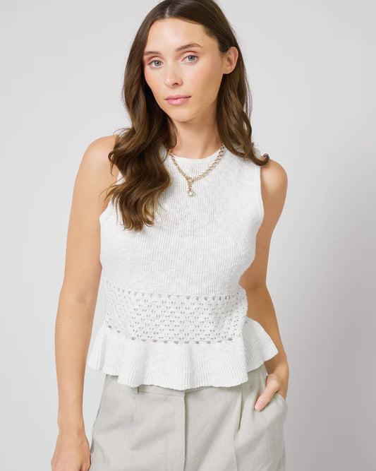 Woman wearing a white peplum top in front of a white background.