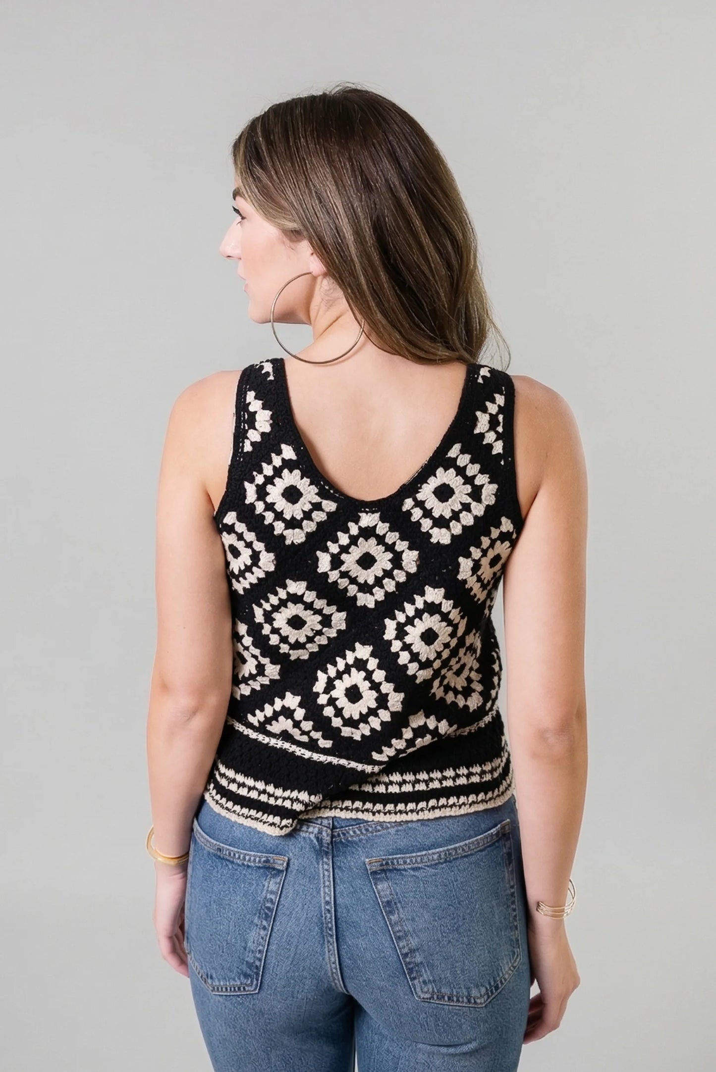 Woman wearing a black and white patterned sleeveless top against a gray background