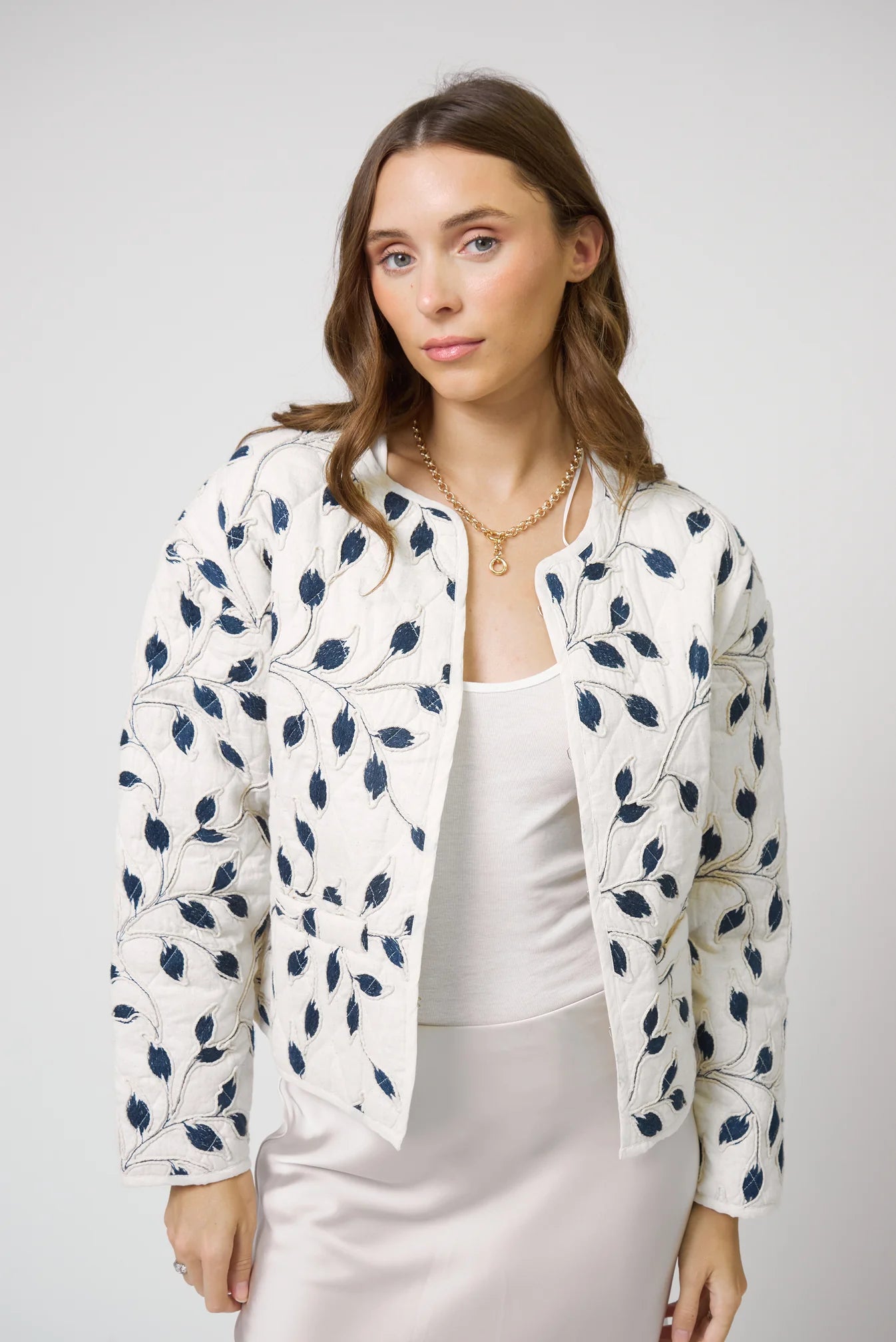 Woman wearing a white jacket with blue floral patterns on a plain background
