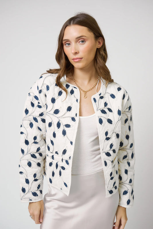 Woman wearing a white jacket with blue floral patterns on a plain background