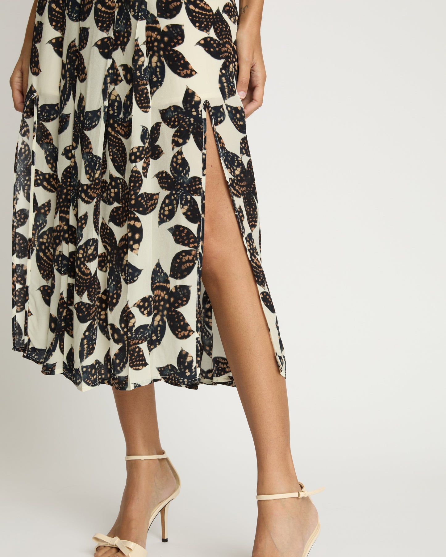 Person wearing a floral dress with a high slit and beige sandals on a white background