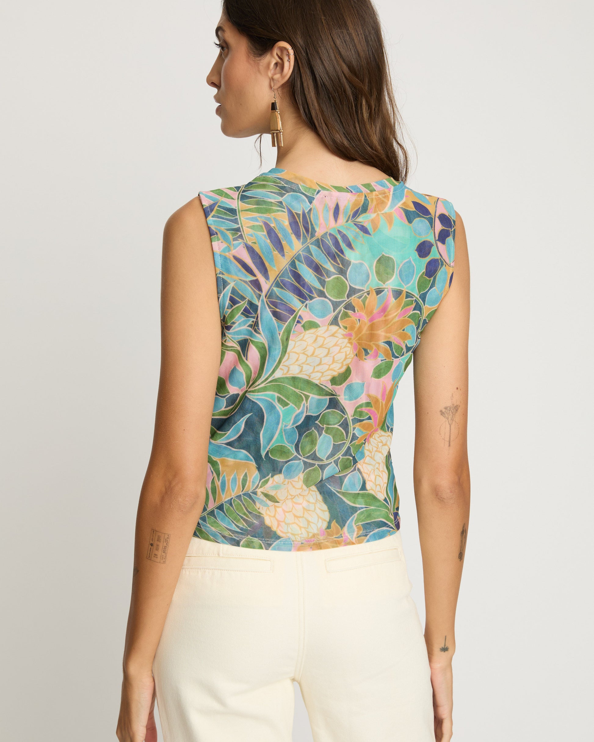 Woman wearing a sleeveless top with a colorful floral pattern on a plain background
