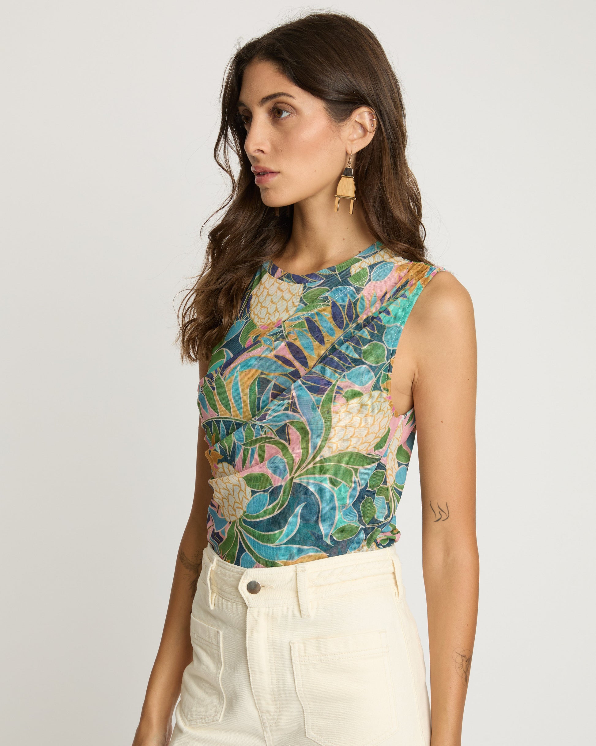 Woman wearing a colorful floral top and white pants on a plain background