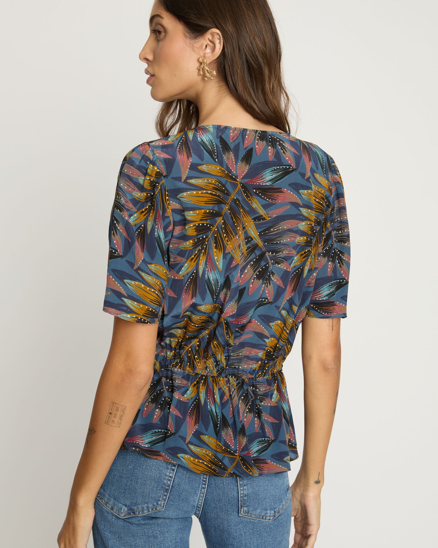 Woman wearing a colorful floral blouse and blue jeans on a plain background