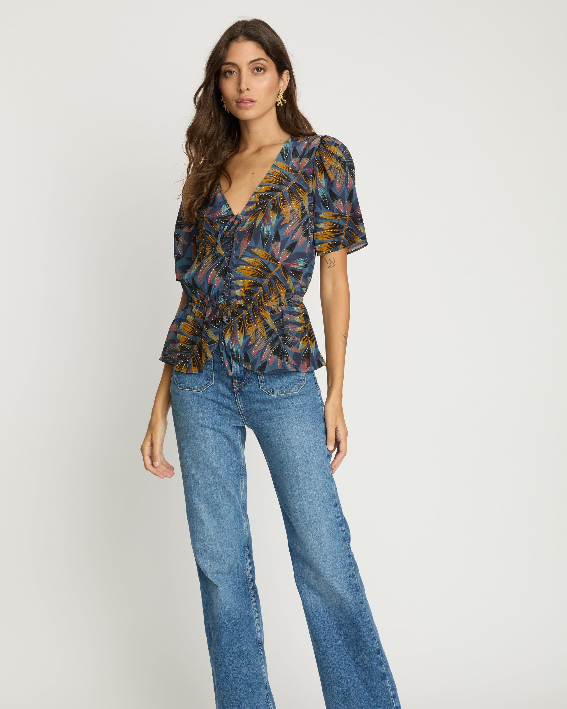 Woman wearing a patterned top and blue jeans on a white background
