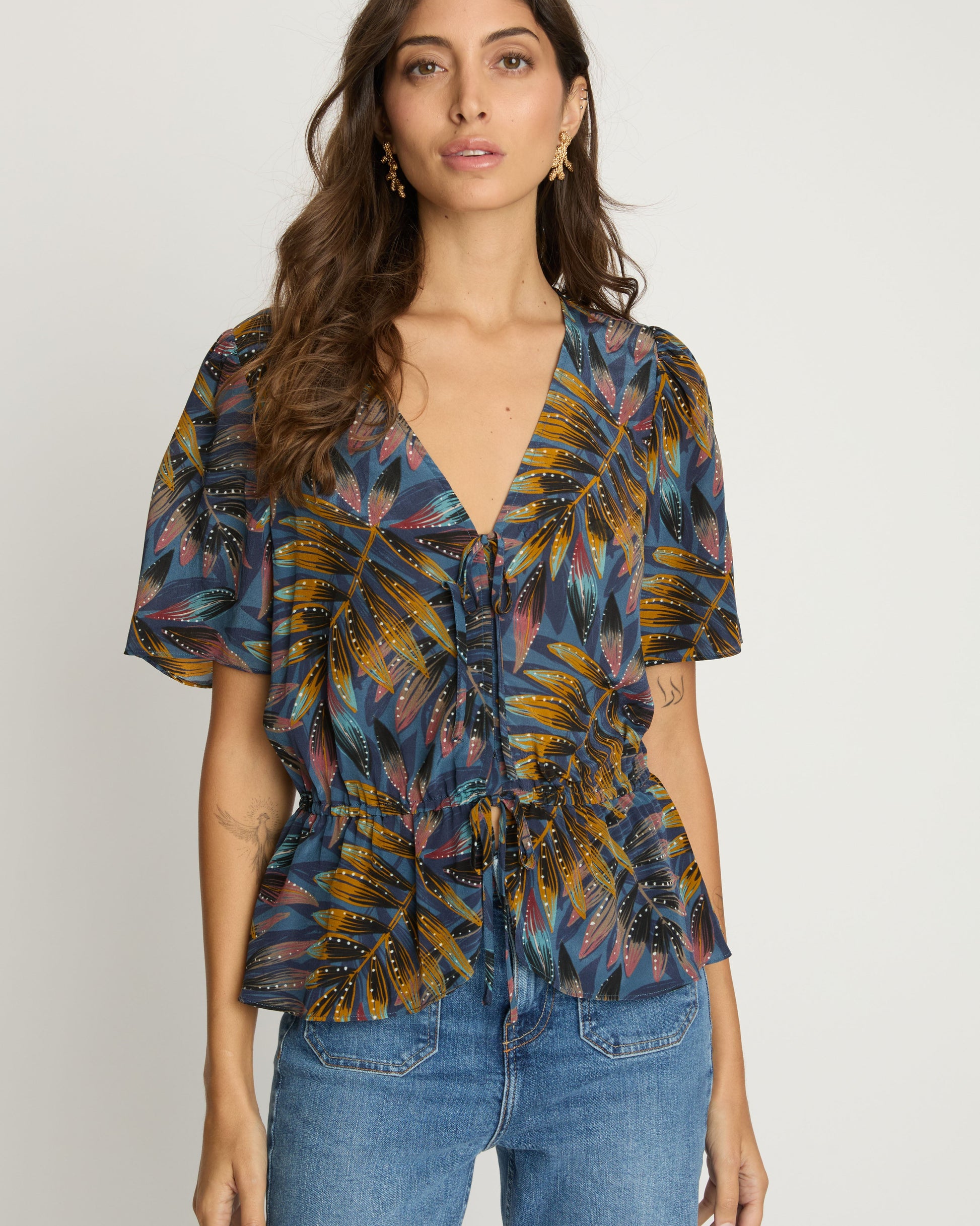Woman wearing a patterned blouse and jeans on a white background