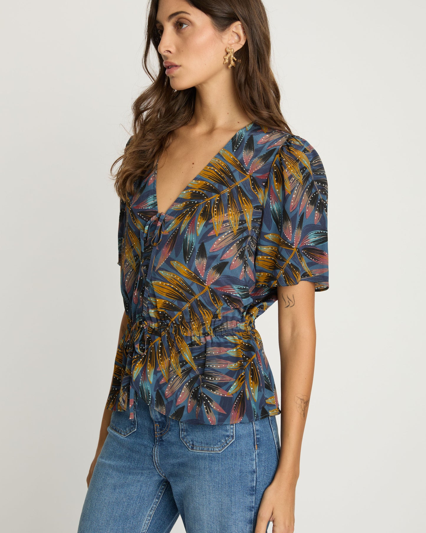 Woman wearing a patterned top and jeans on a plain background
