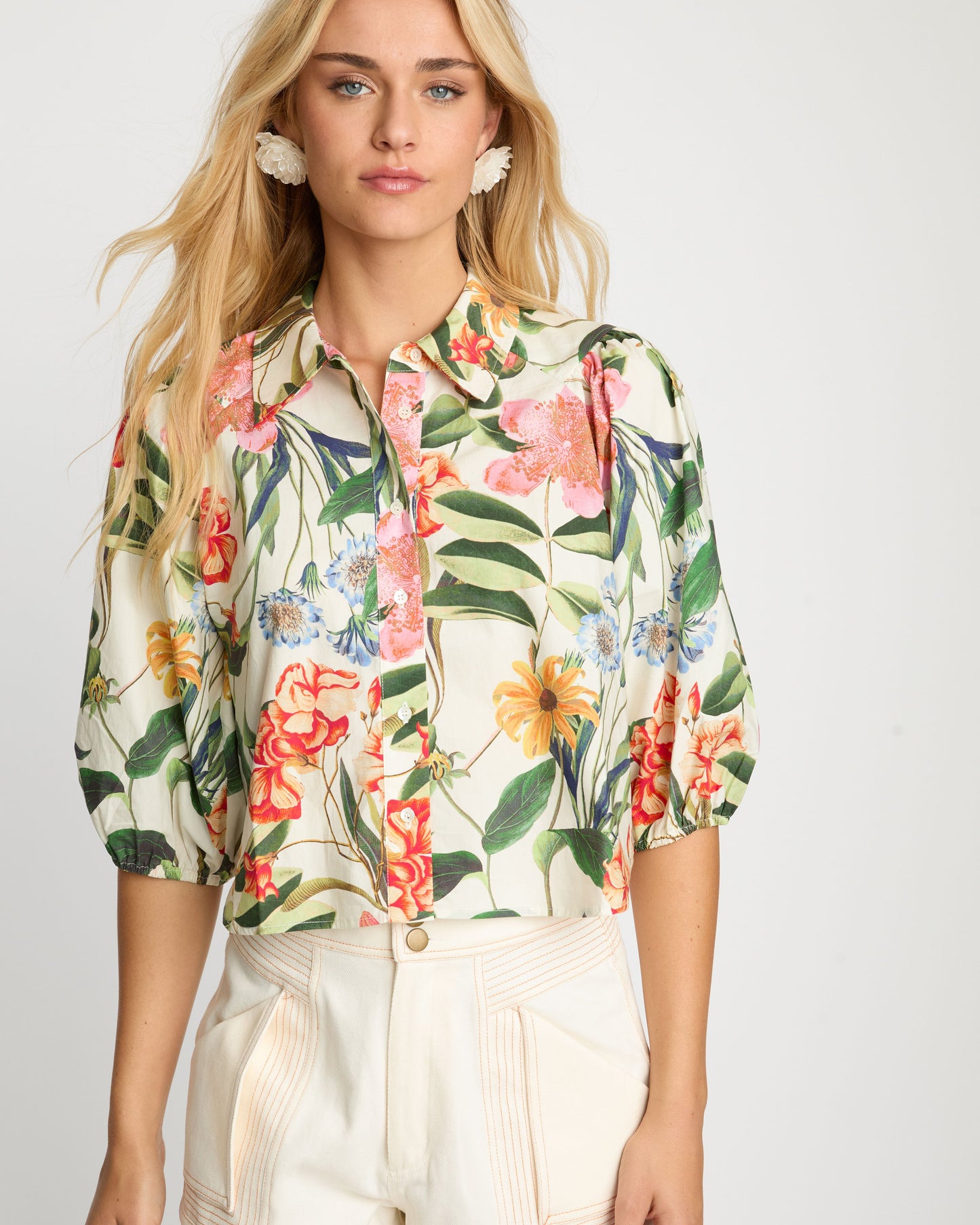 Woman wearing a floral blouse and beige shorts on a white background