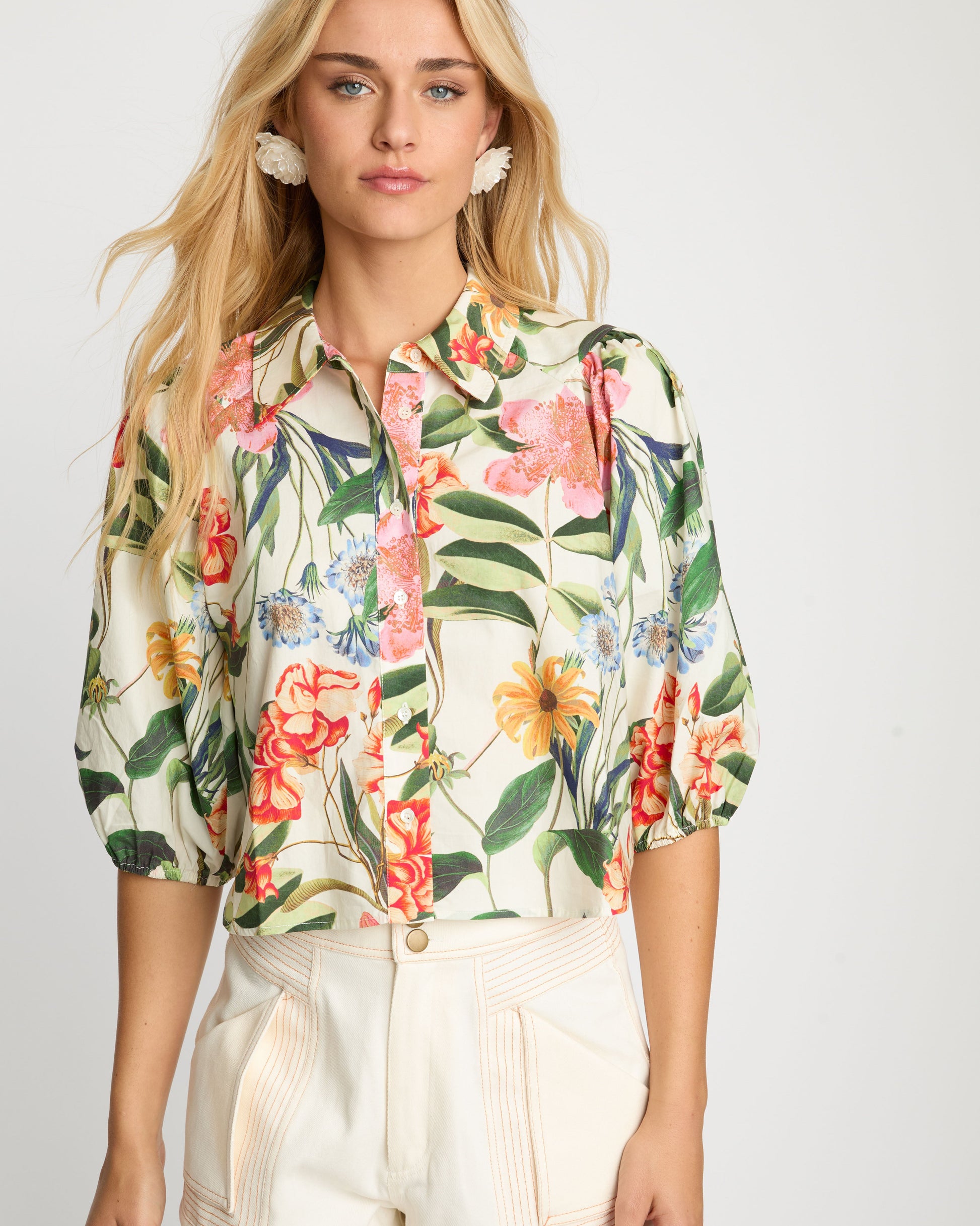 Woman wearing a floral blouse and beige shorts on a white background