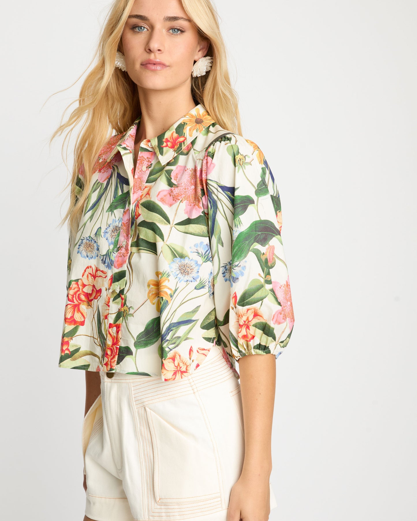 Woman wearing a floral blouse and beige shorts on a white background