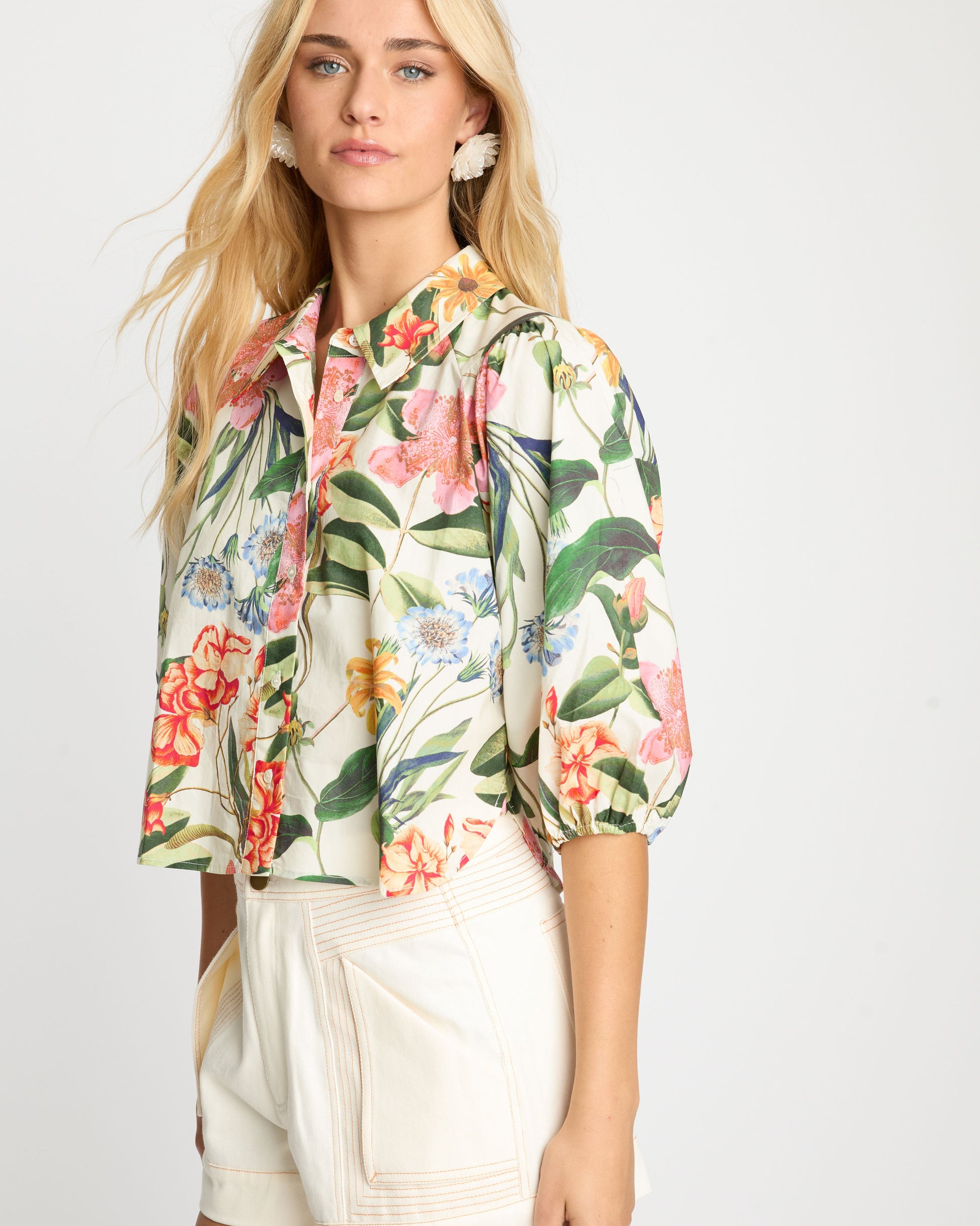 Woman wearing a floral blouse and beige shorts on a white background