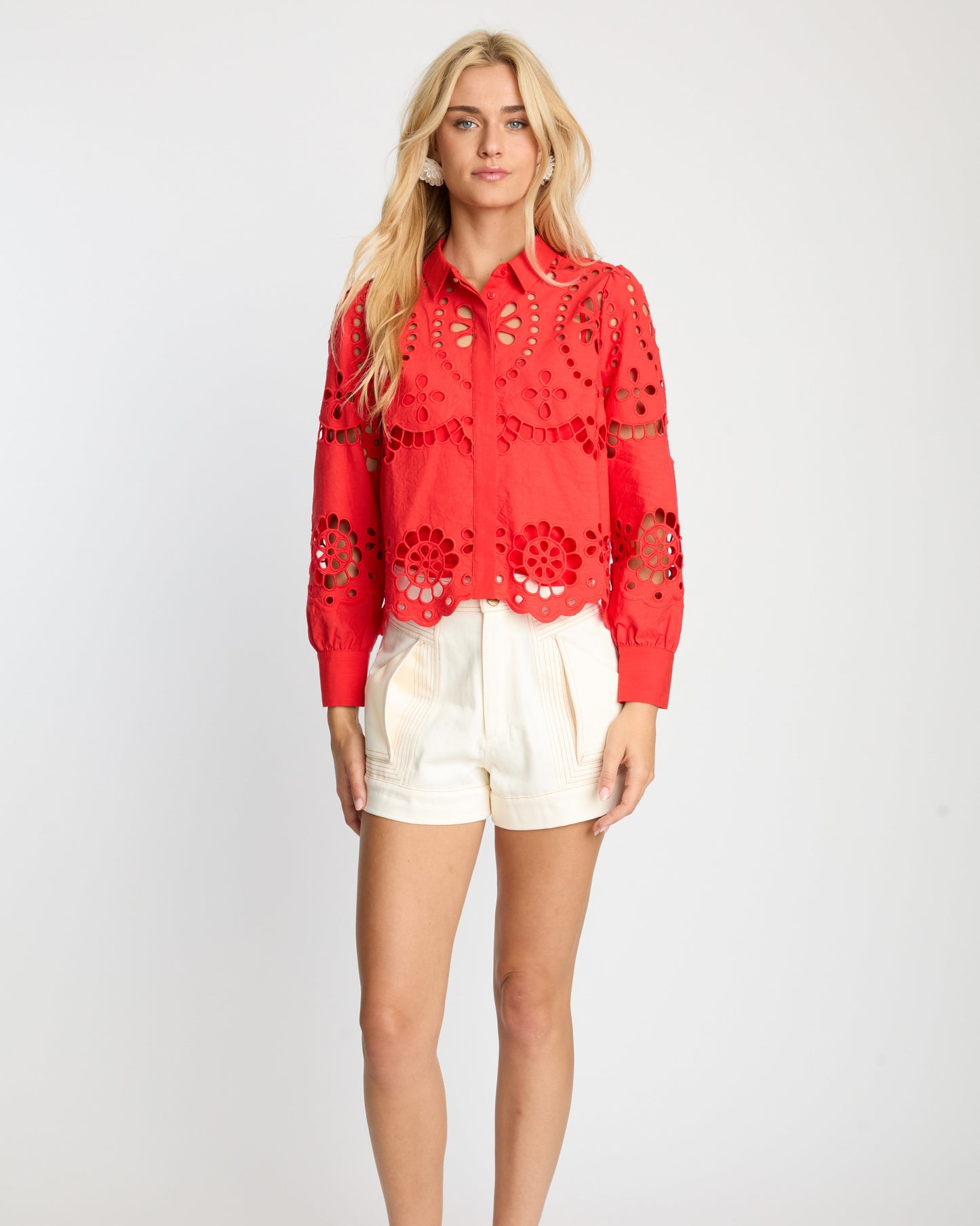 Woman wearing a red lace top and white shorts on a white background