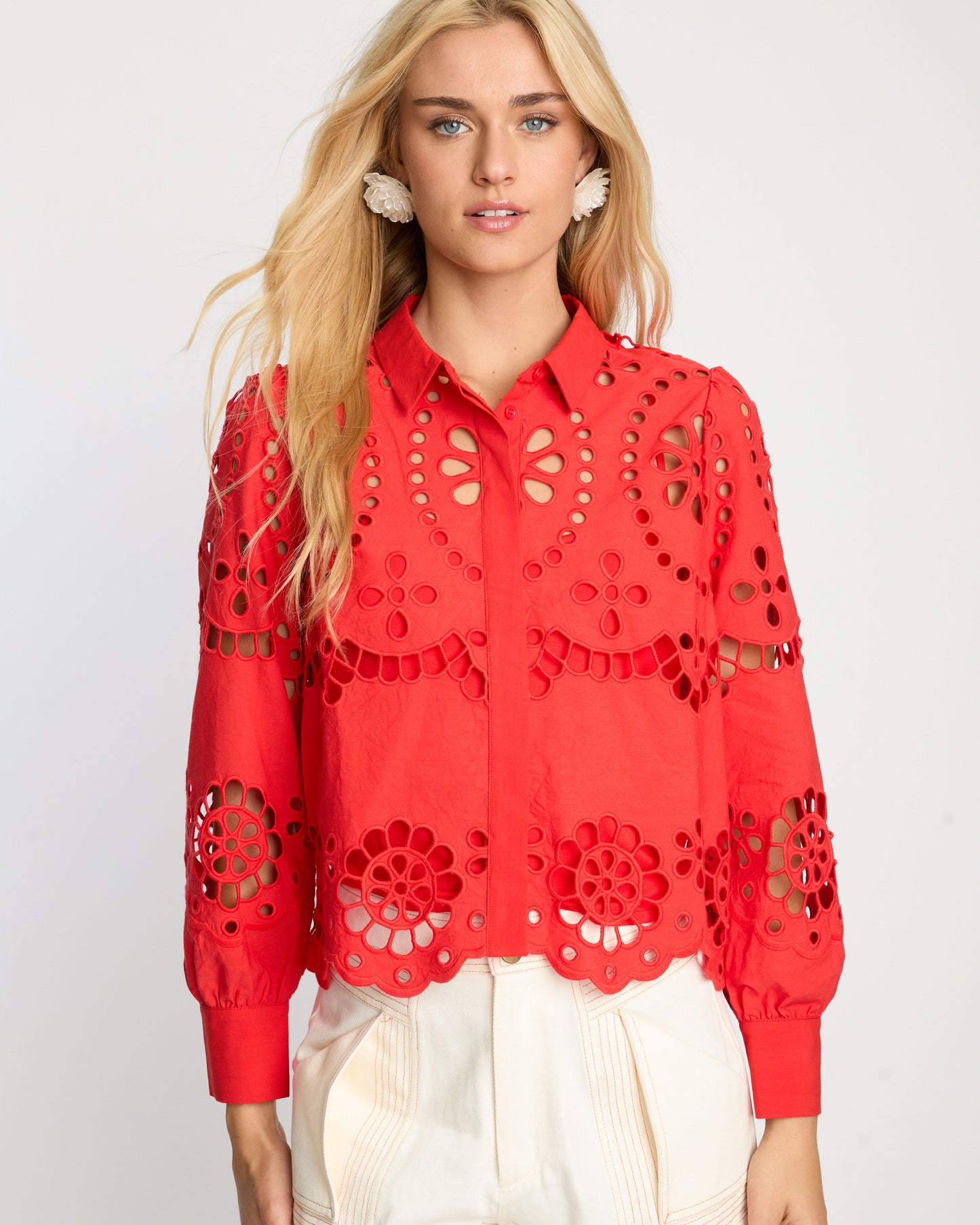 Woman wearing a red lace blouse and white shorts on a plain background