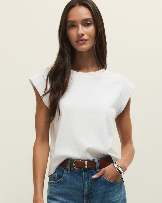 Woman wearing a white sleeveless top and blue jeans against a plain background