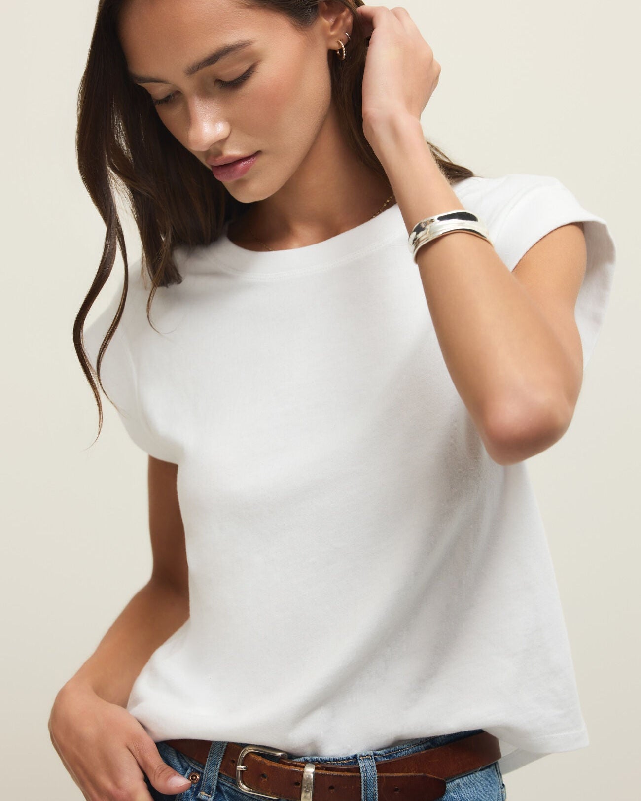 Woman wearing a white t-shirt and blue jeans against a plain background