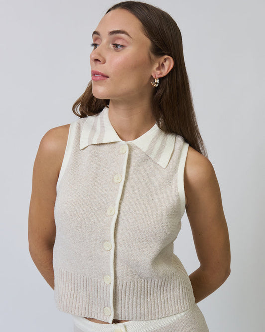 Woman wearing a beige sleeveless knit cardigan over a white shirt against a plain background
