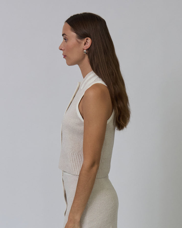 Woman wearing a beige sleeveless top and skirt set against a plain background