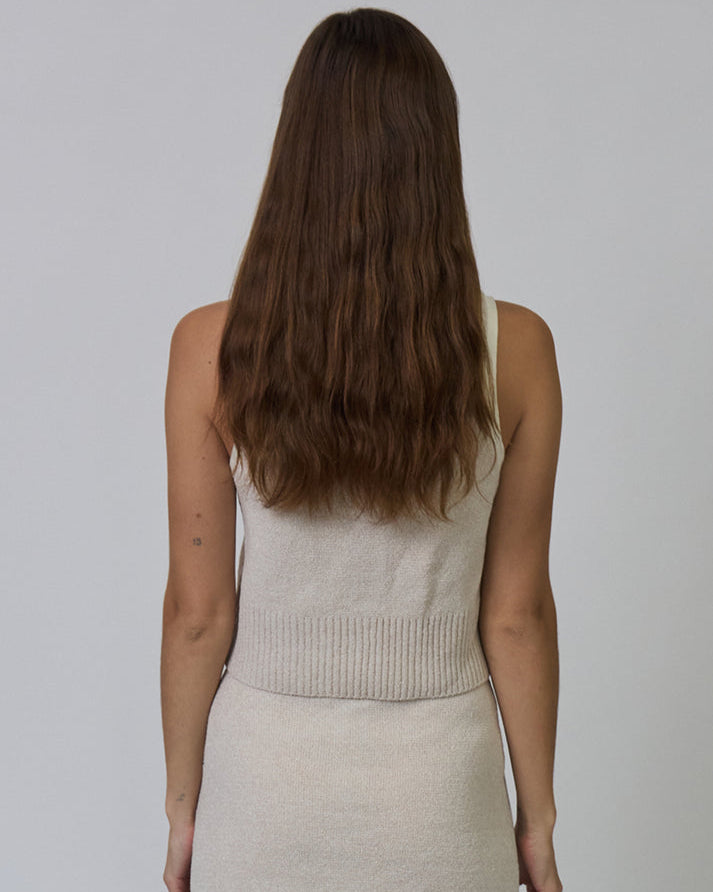 Woman wearing a beige sleeveless top and skirt set against a plain background
