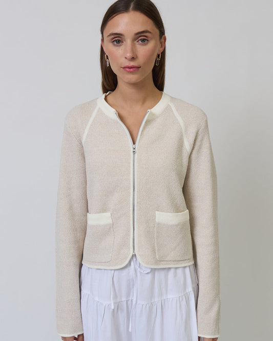 Woman wearing a beige zip-up cardigan over a white dress against a plain background