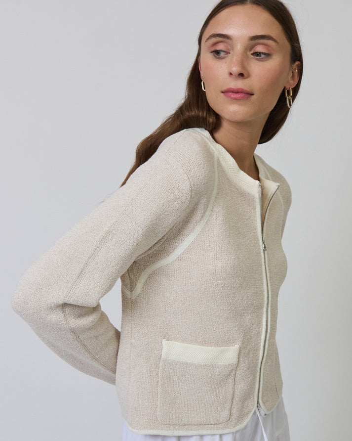 Woman wearing a beige zip-up jacket with a pocket on a plain background