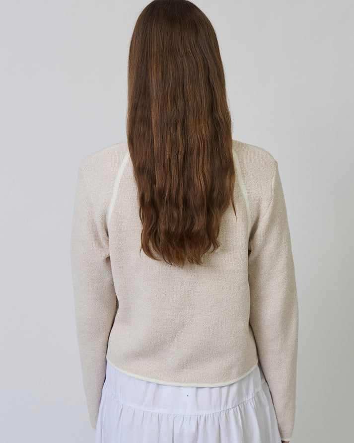 Person wearing a beige cardigan and white skirt against a plain background