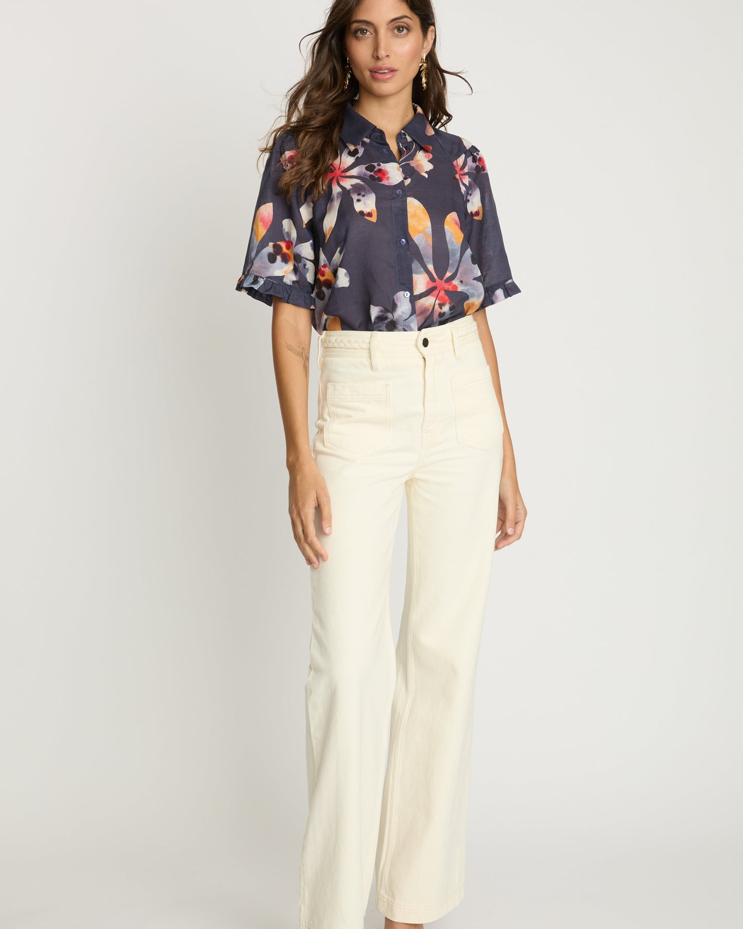 Woman wearing a floral blouse and white pants on a white background