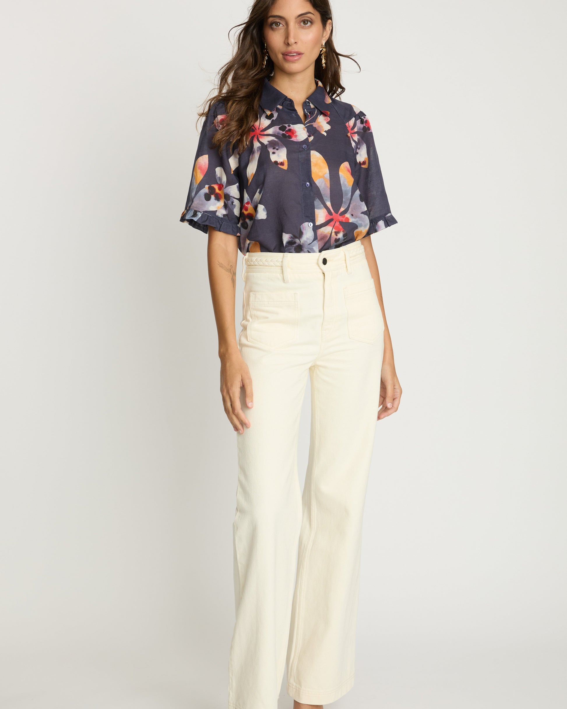 Woman wearing a floral blouse and white pants on a white background