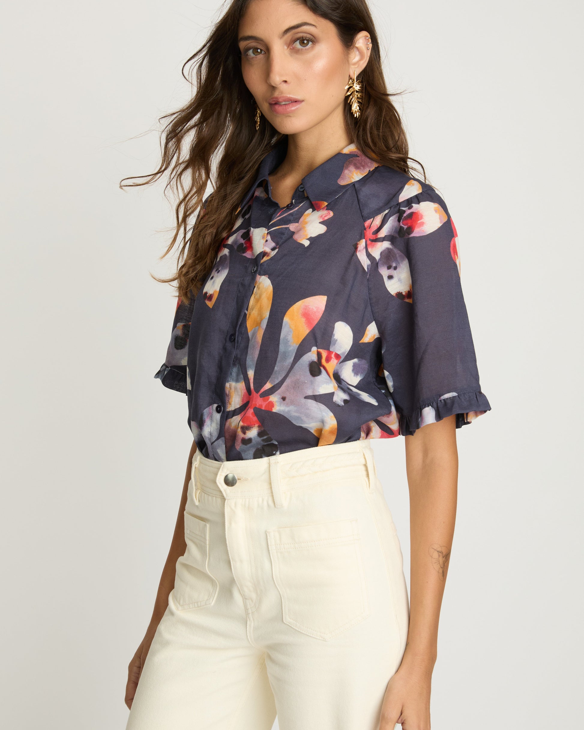 Woman wearing a floral blouse and white pants on a plain background