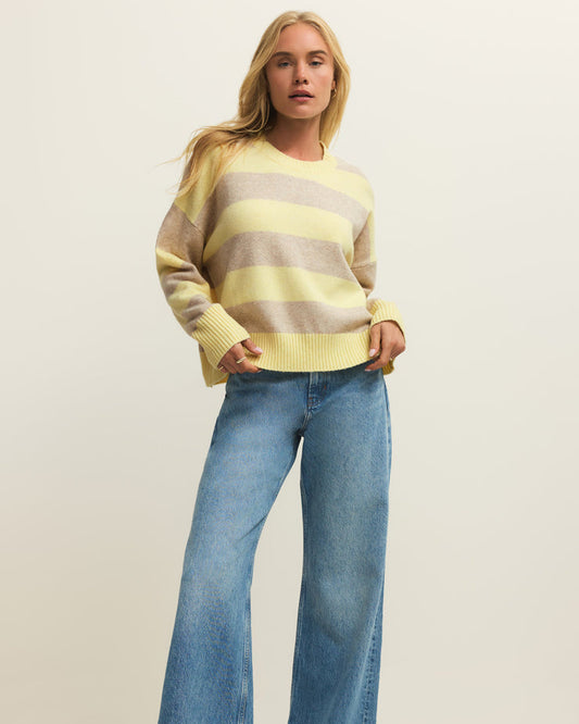 Woman wearing a striped sweater and blue jeans on a plain background